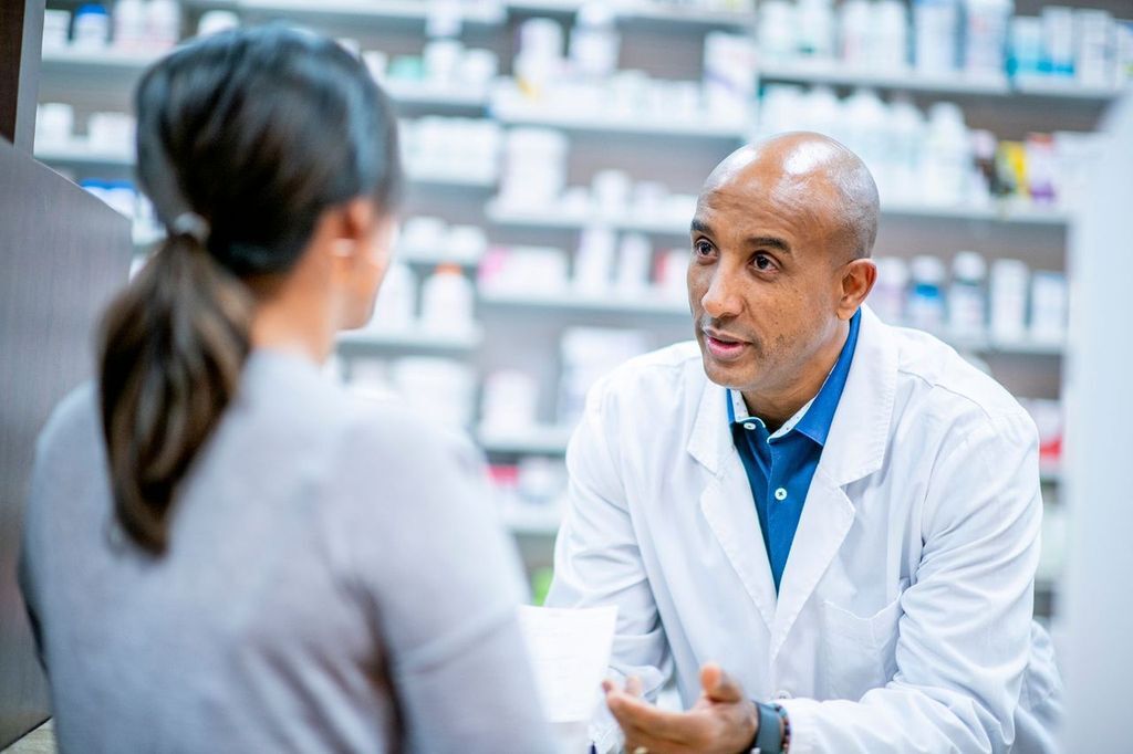 A clinical pharmacist or specialty pharmacist consulting with a patient or provider in a private or semi-private setting — medication counseling, chart review, or discussing complex therapies.