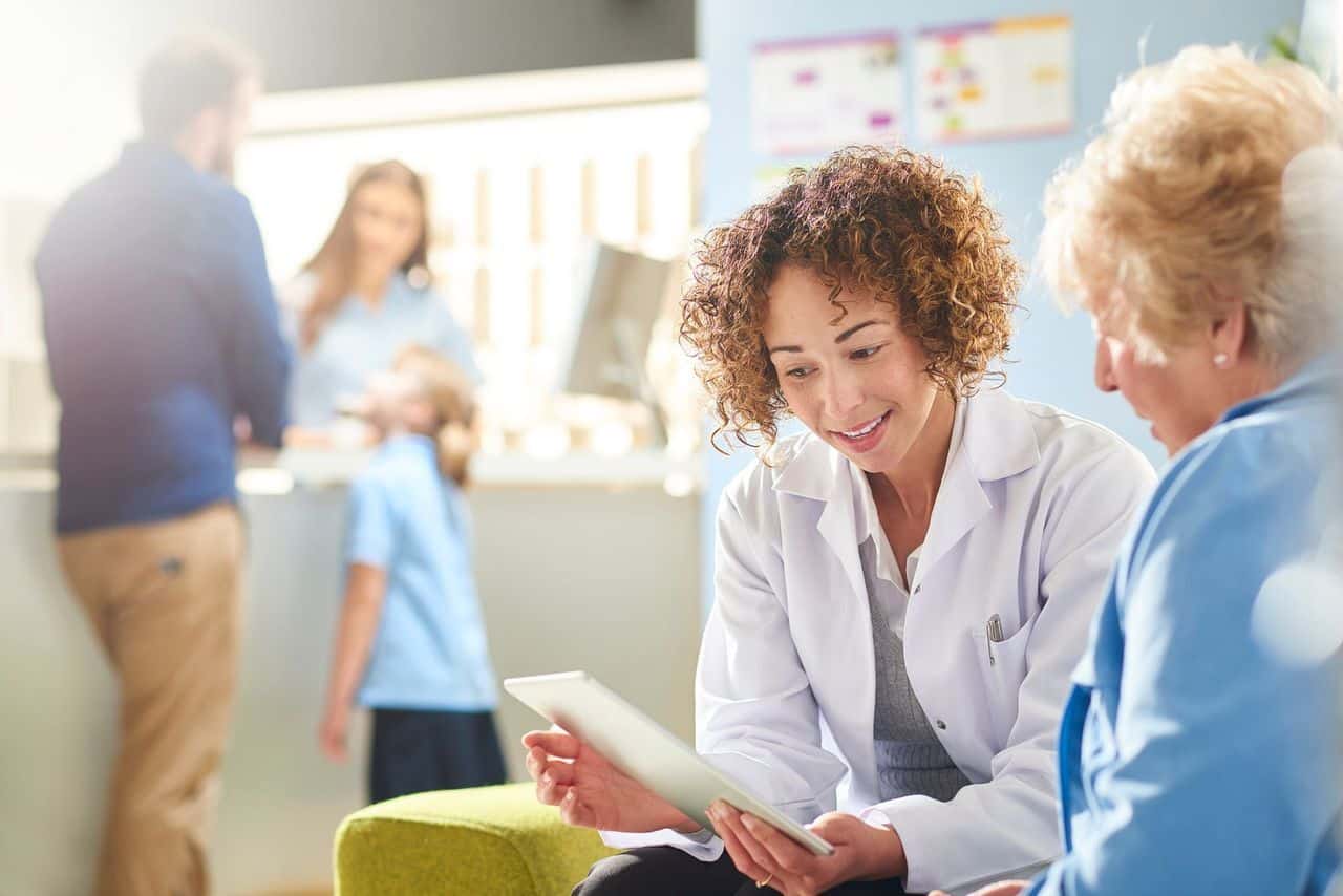 A clinical pharmacist or pharmacy director sitting with a patient or provider, reviewing a chart or medication plan in a calm, professional clinic setting.